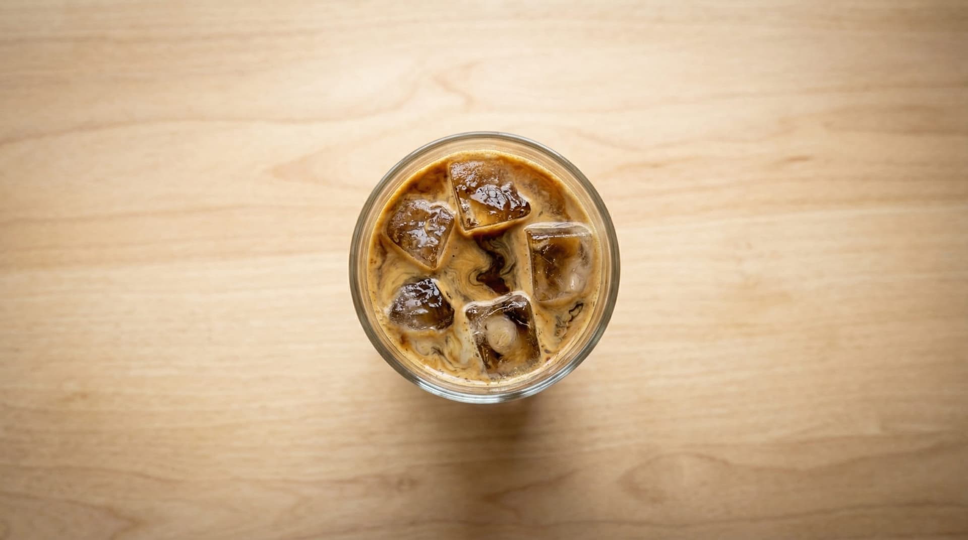 Homemade iced latte in a tall glass with dark espresso pooling through cold milk and ice cubes on a wooden café counter — cold latte recipe
