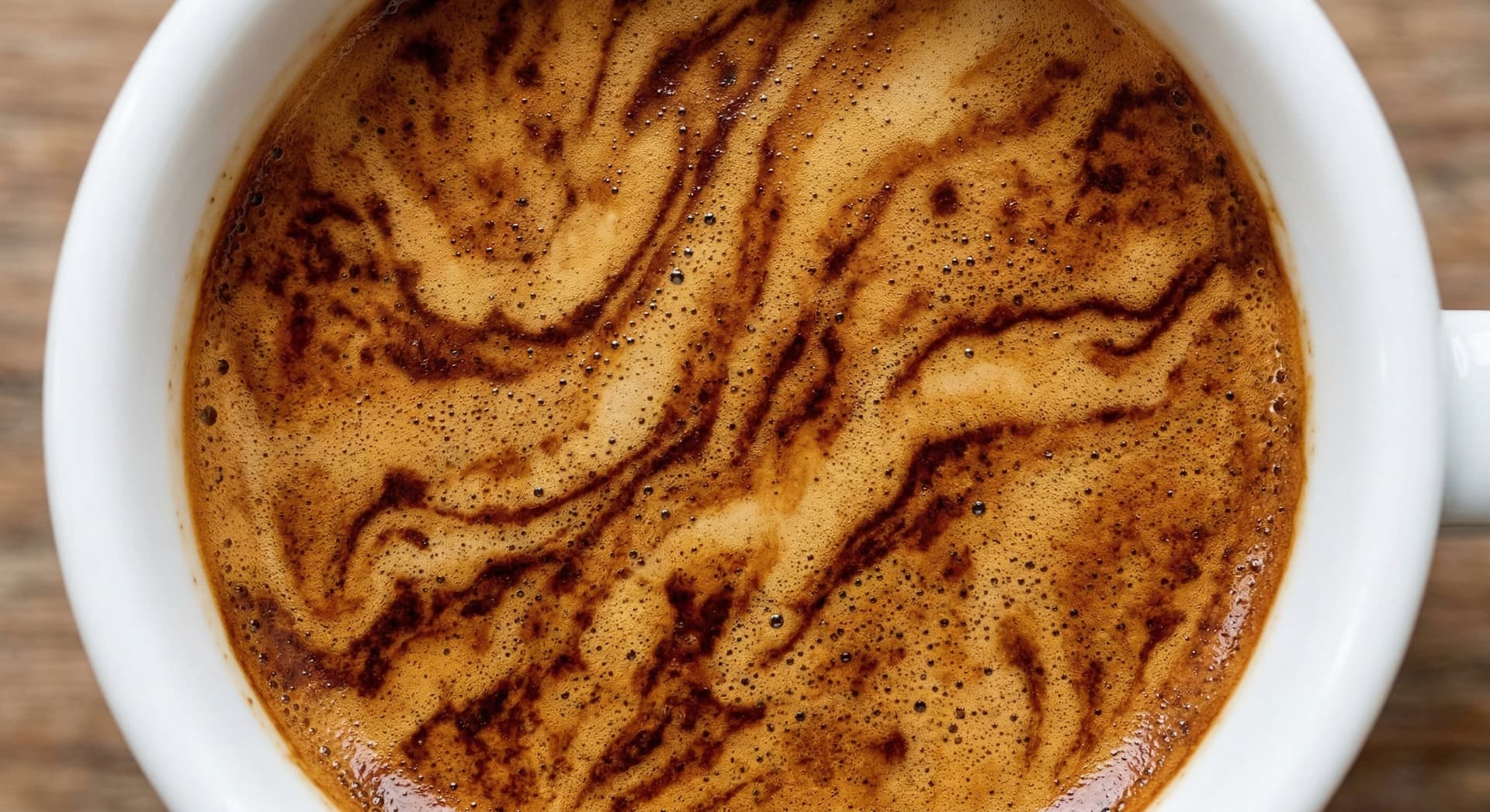 Macro top-down photography of espresso crema surface showing tiger stripe pattern — dark reddish-brown streaks alternating with golden hazelnut zones on freshly extracted espresso