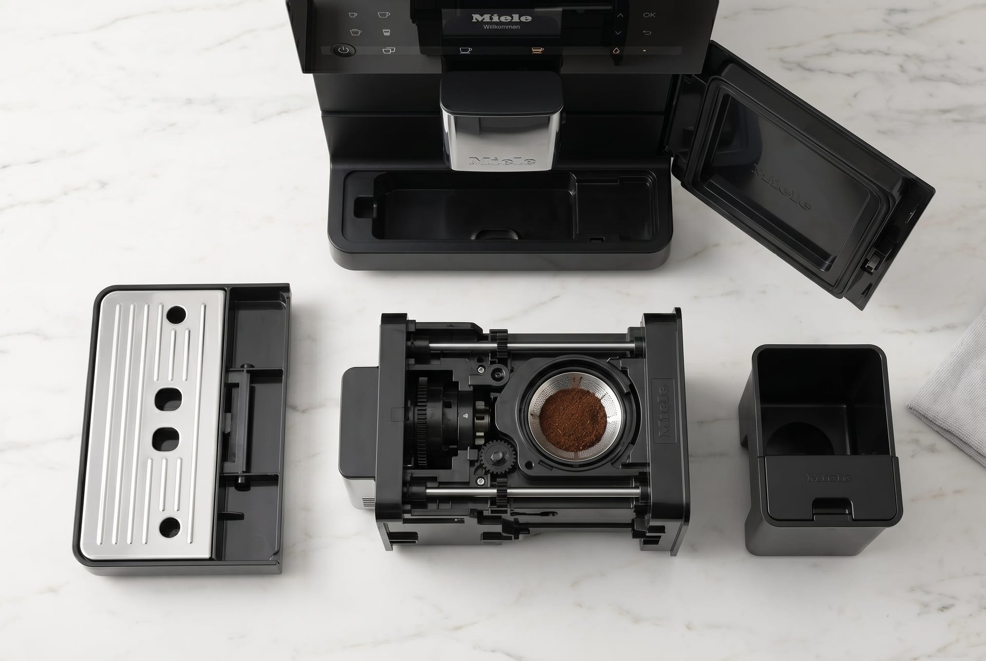 Miele CM 5310 Silence removable brew unit shown pulled out for daily cleaning alongside drip tray and grounds container for easy miele automatic coffee maker maintenance