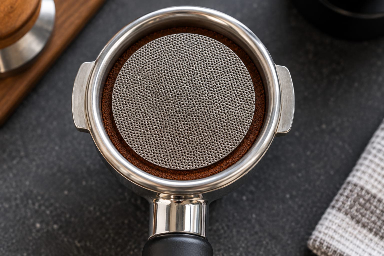 A stainless steel puck screen placed on top of a tamped espresso puck inside a portafilter basket before brewing