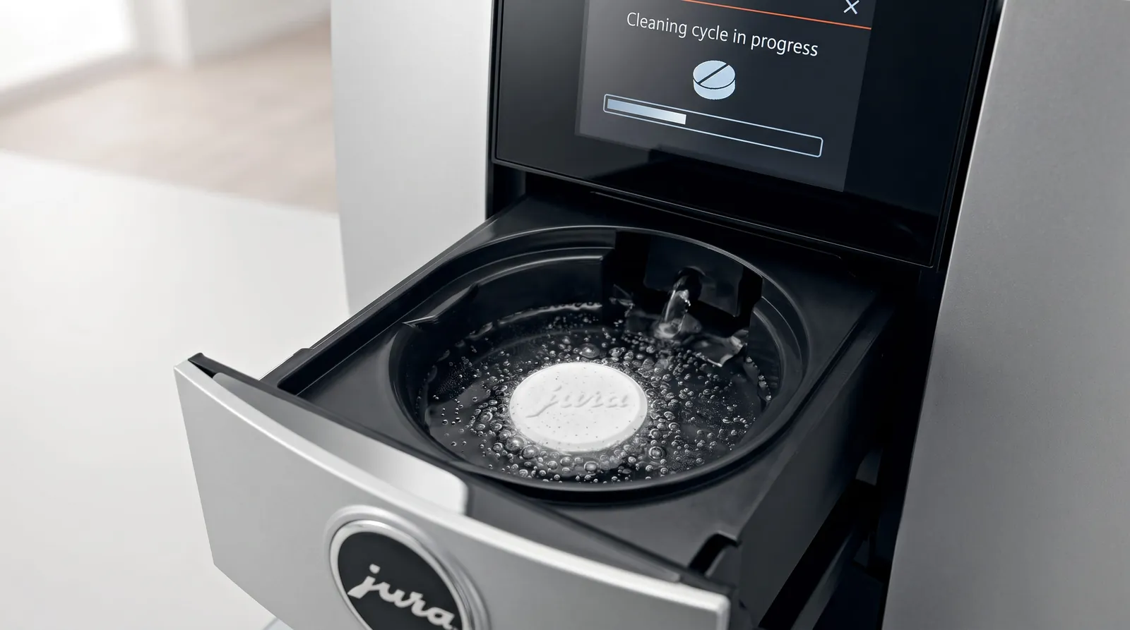 Cleaning tablet dissolving in the brew chamber of a bean-to-cup coffee machine while the display shows a cleaning cycle in progress