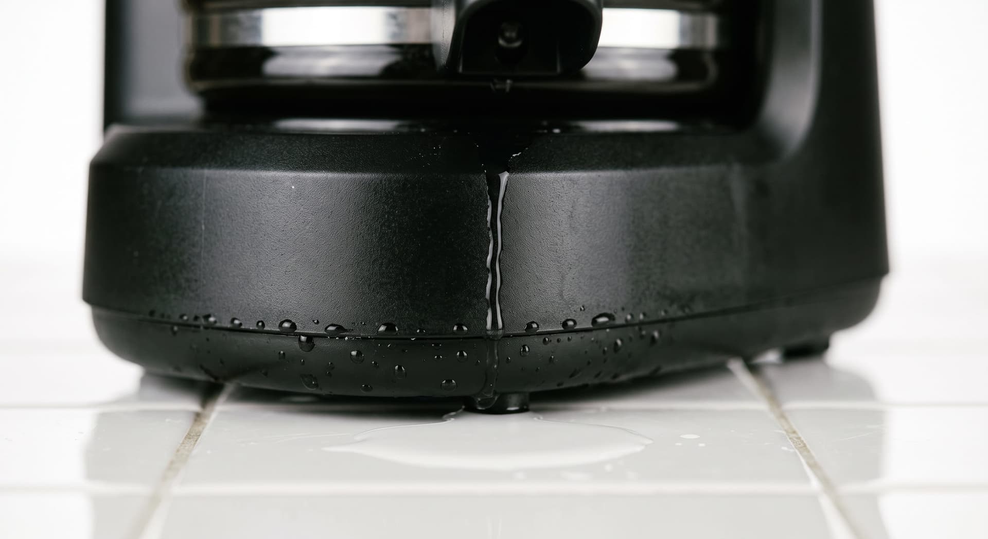 Water pooling on a kitchen counter directly beneath a drip coffee maker — illustrating a coffee maker leaking from the bottom near the heating element base