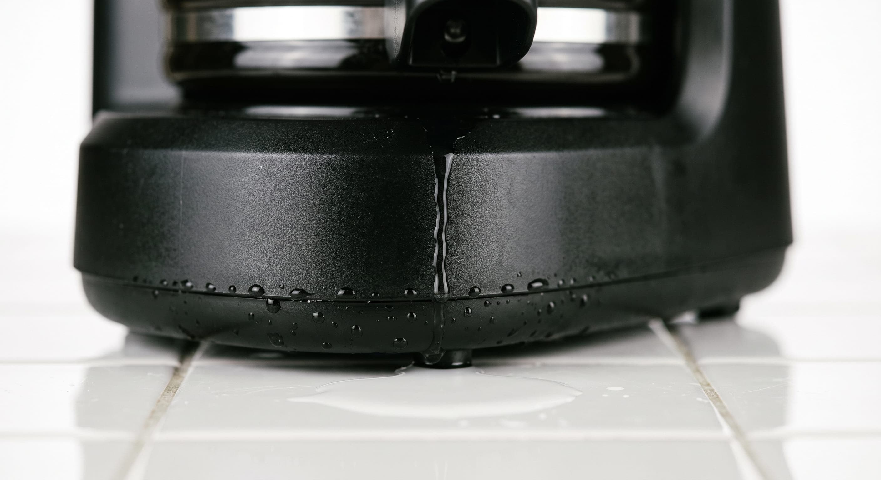 Water pooling on a kitchen counter directly beneath a drip coffee maker — illustrating a coffee maker leaking from the bottom near the heating element base