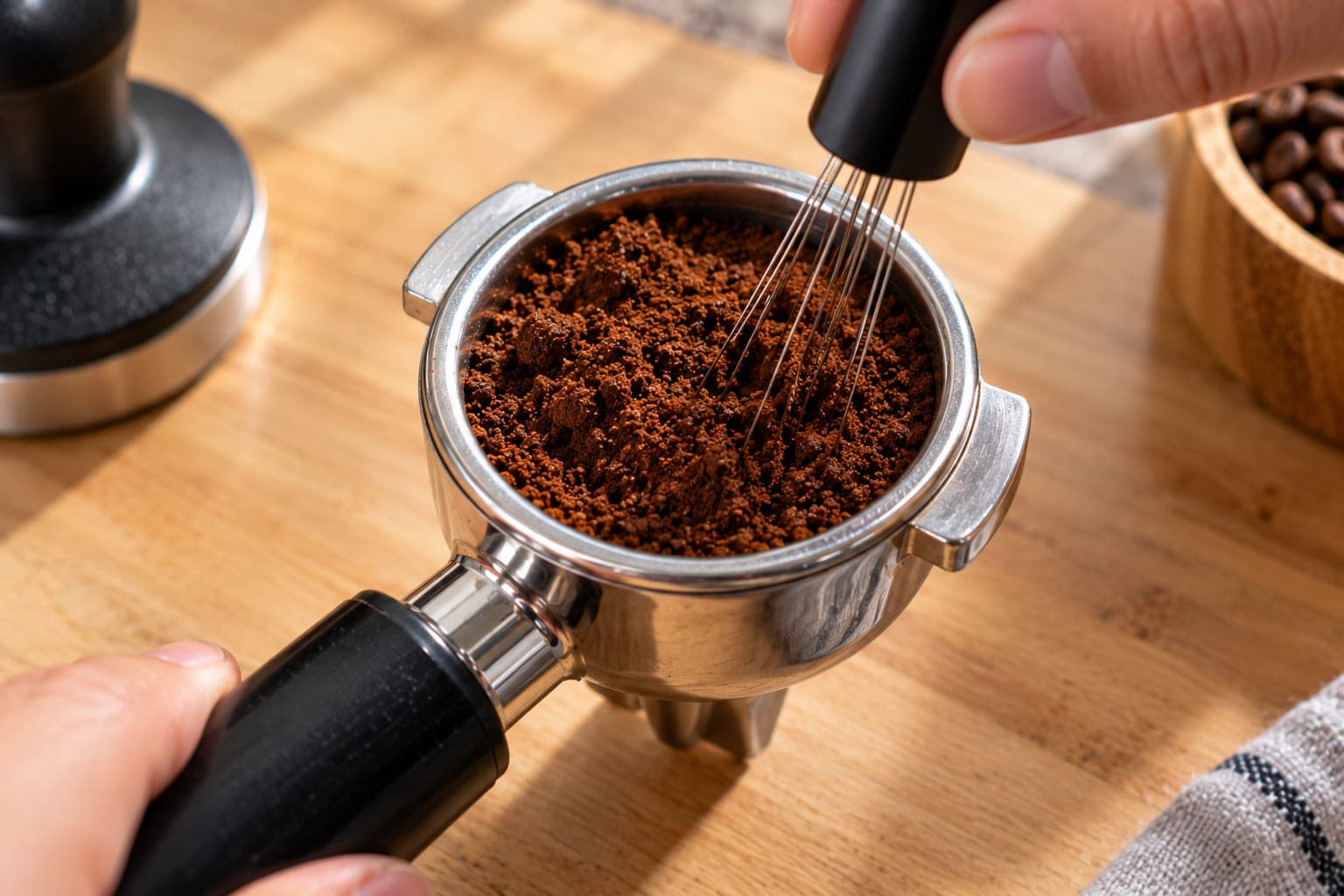A WDT tool with fine needles being used to break up clumps and evenly distribute coffee grounds in a portafilter basket before tamping