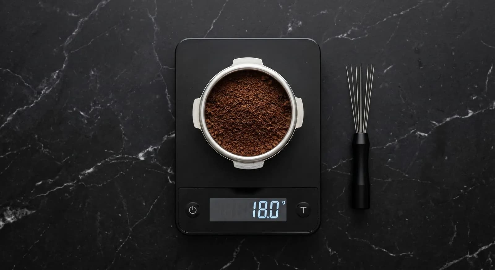 Portafilter of ground coffee on a digital scale reading 18.0 g, with a WDT tool beside it