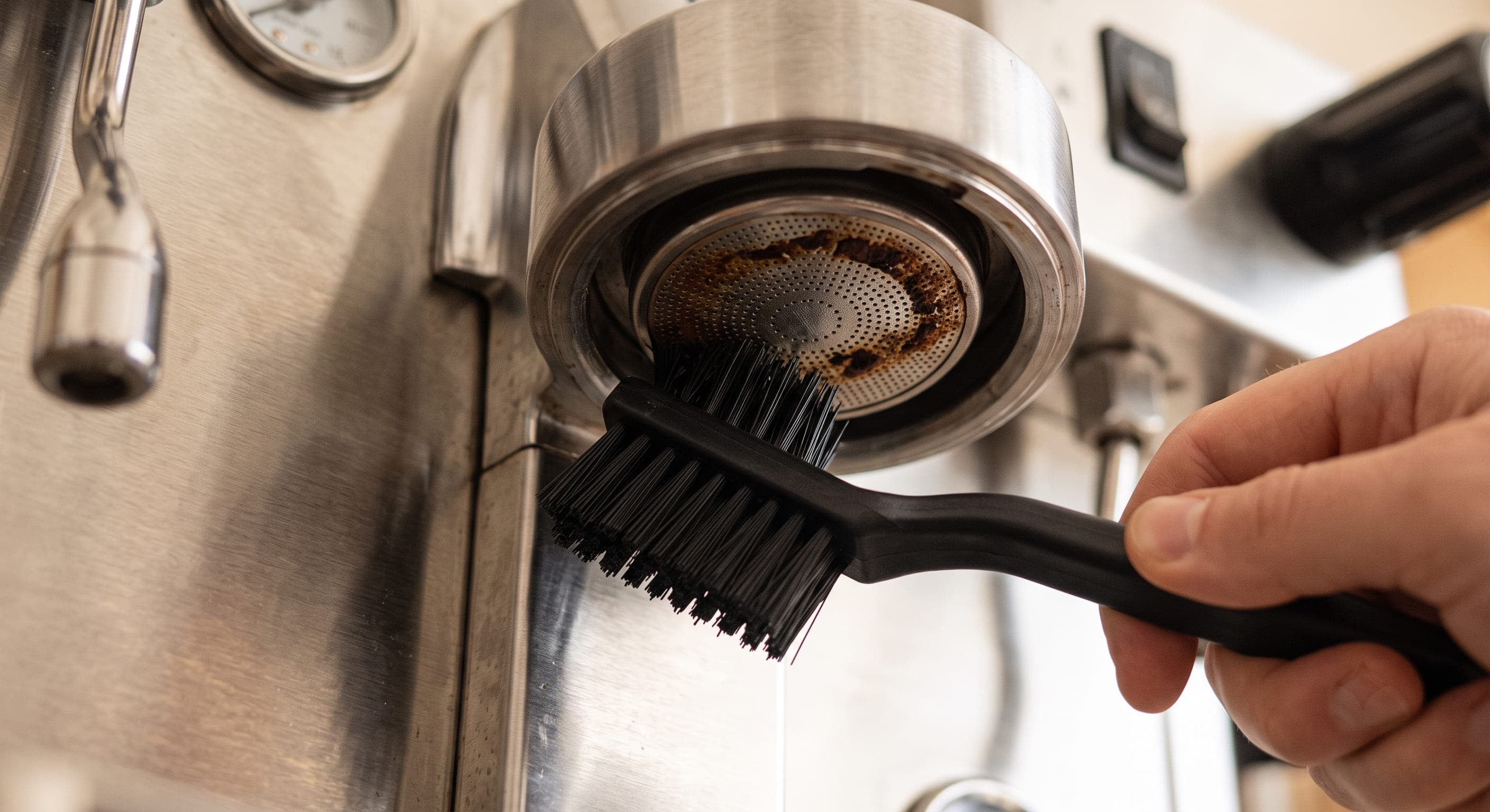 Group head shower screen removed and soaking in a cup of hot water with cleaning tablet — deep cleaning espresso machine group head to restore even water distribution and improve crema quality