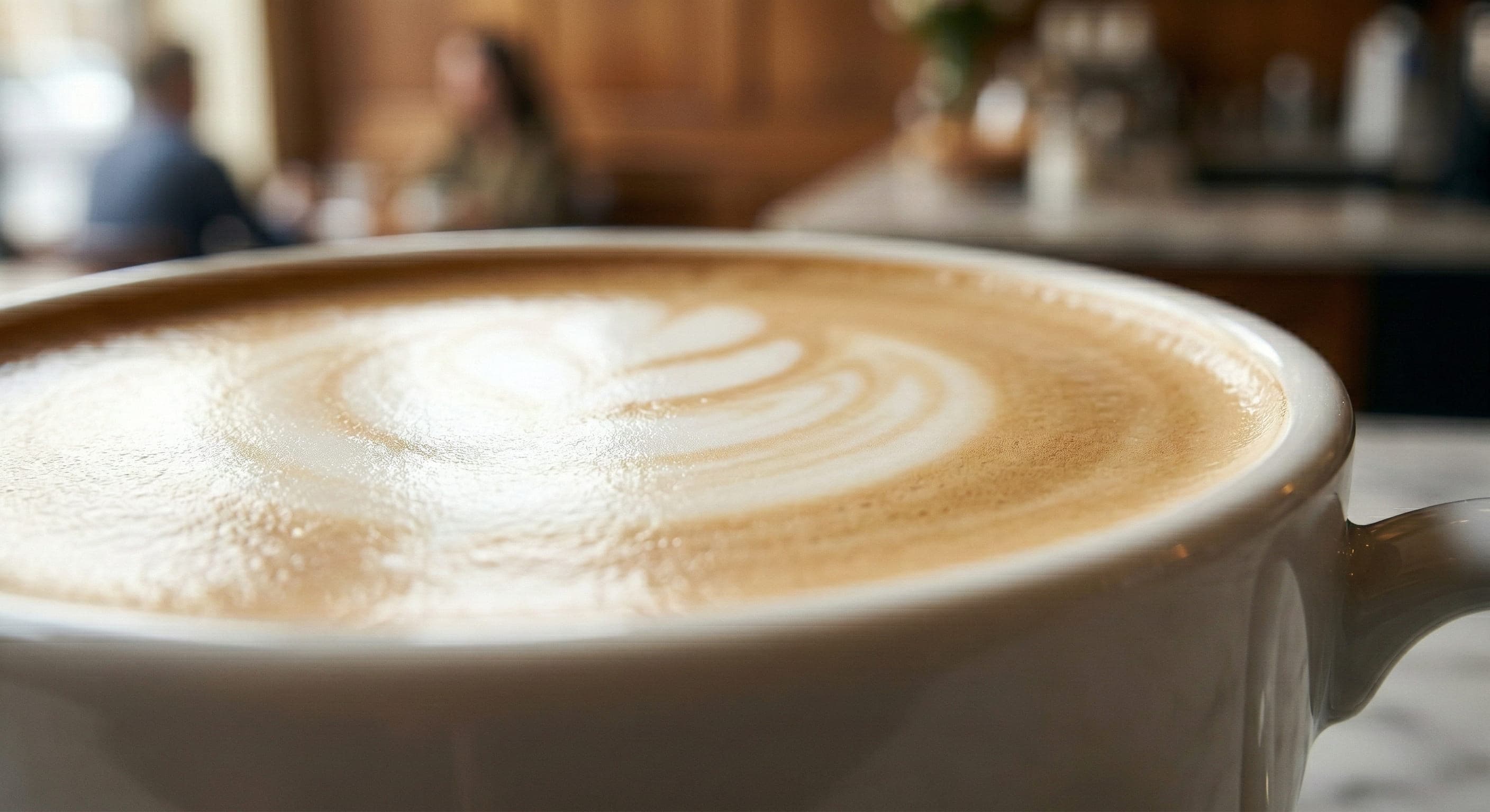 Extreme close-up of flat white microfoam texture in a white ceramic cup showing the glossy, paint-like surface of well-textured milk with no visible bubbles