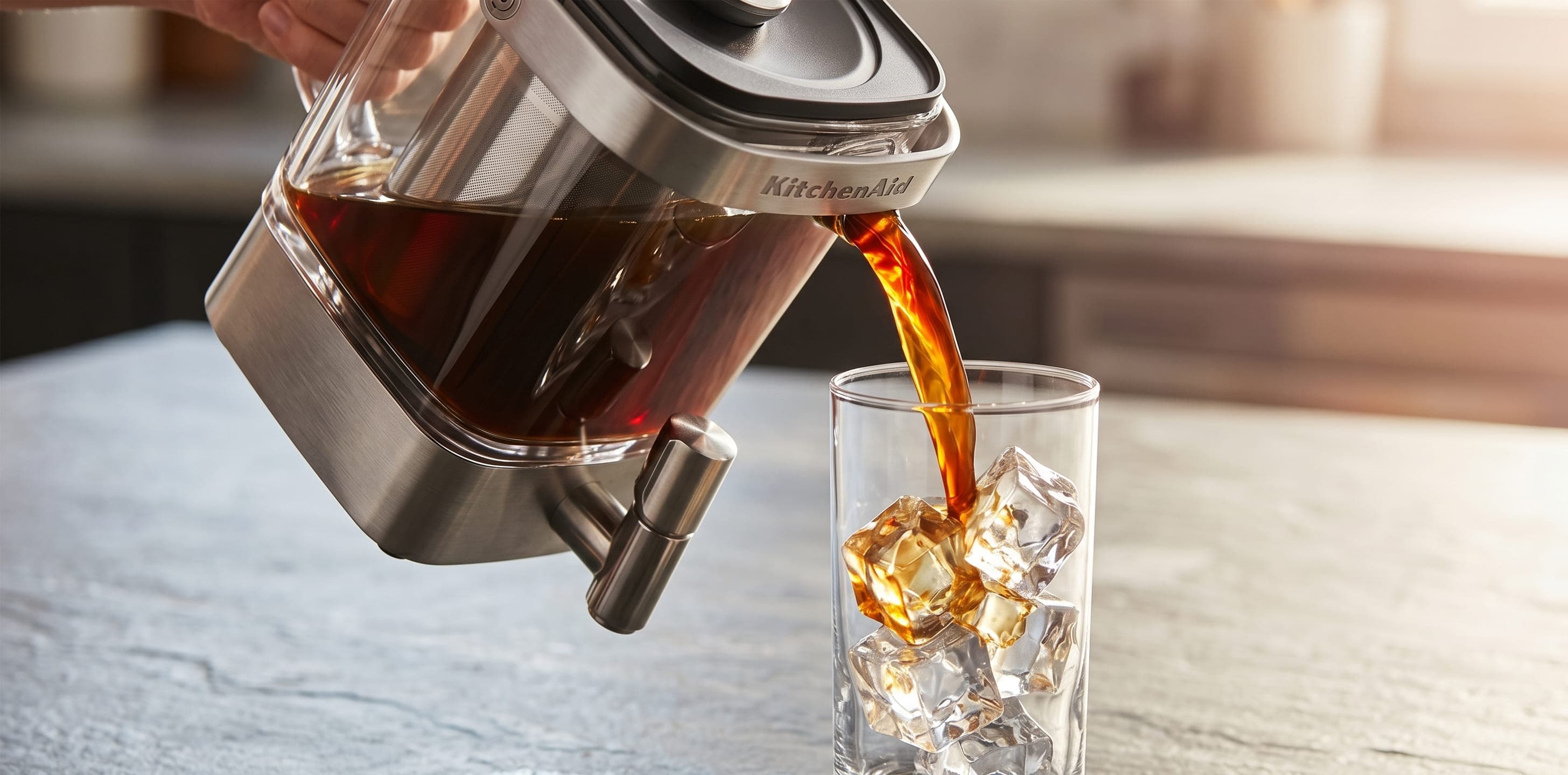 KitchenAid cold brew maker pouring dark concentrate from the glass carafe into an iced glass