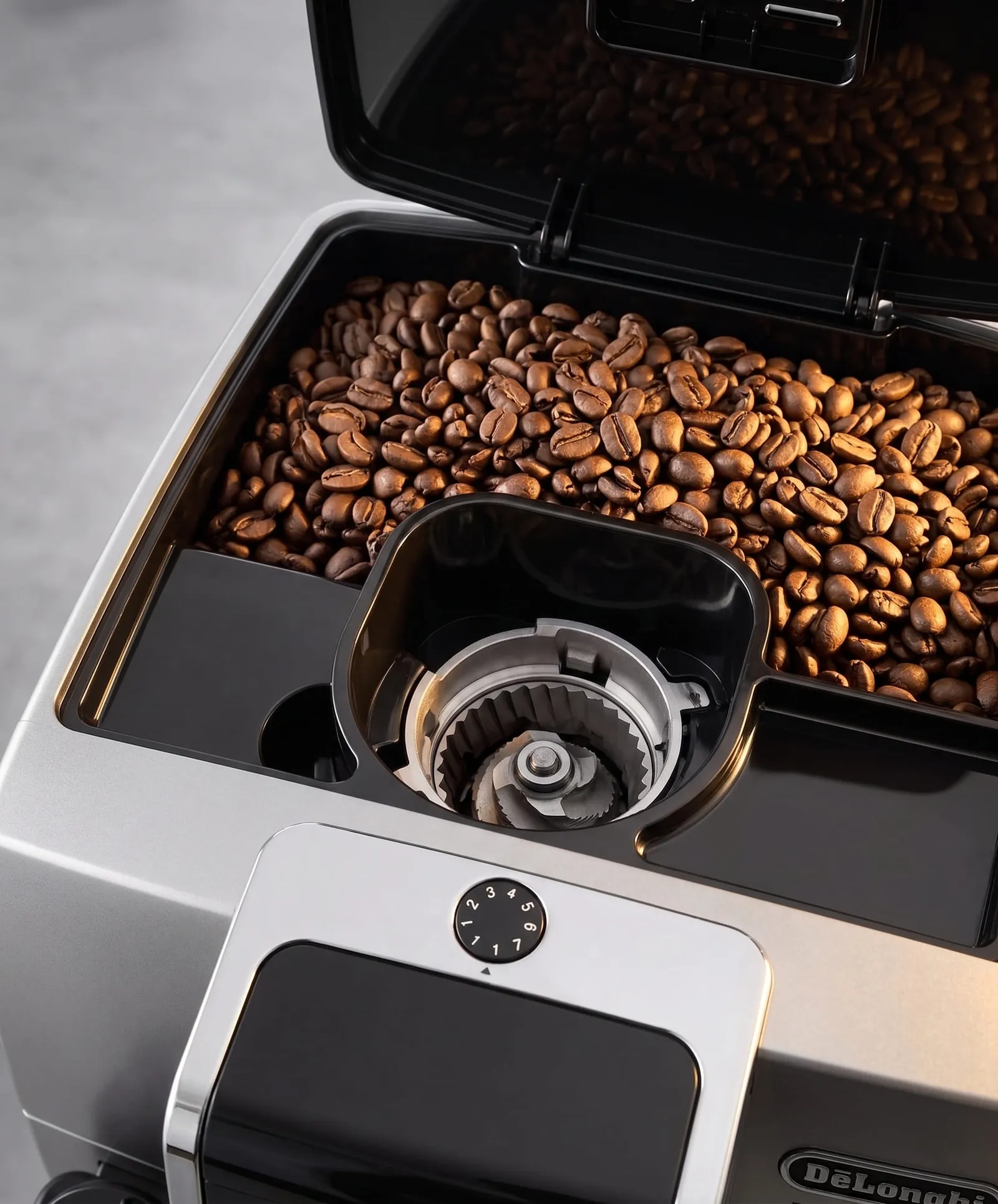 De'Longhi Dinamica Plus open bean hopper above the conical burr grinder and its grind setting dial