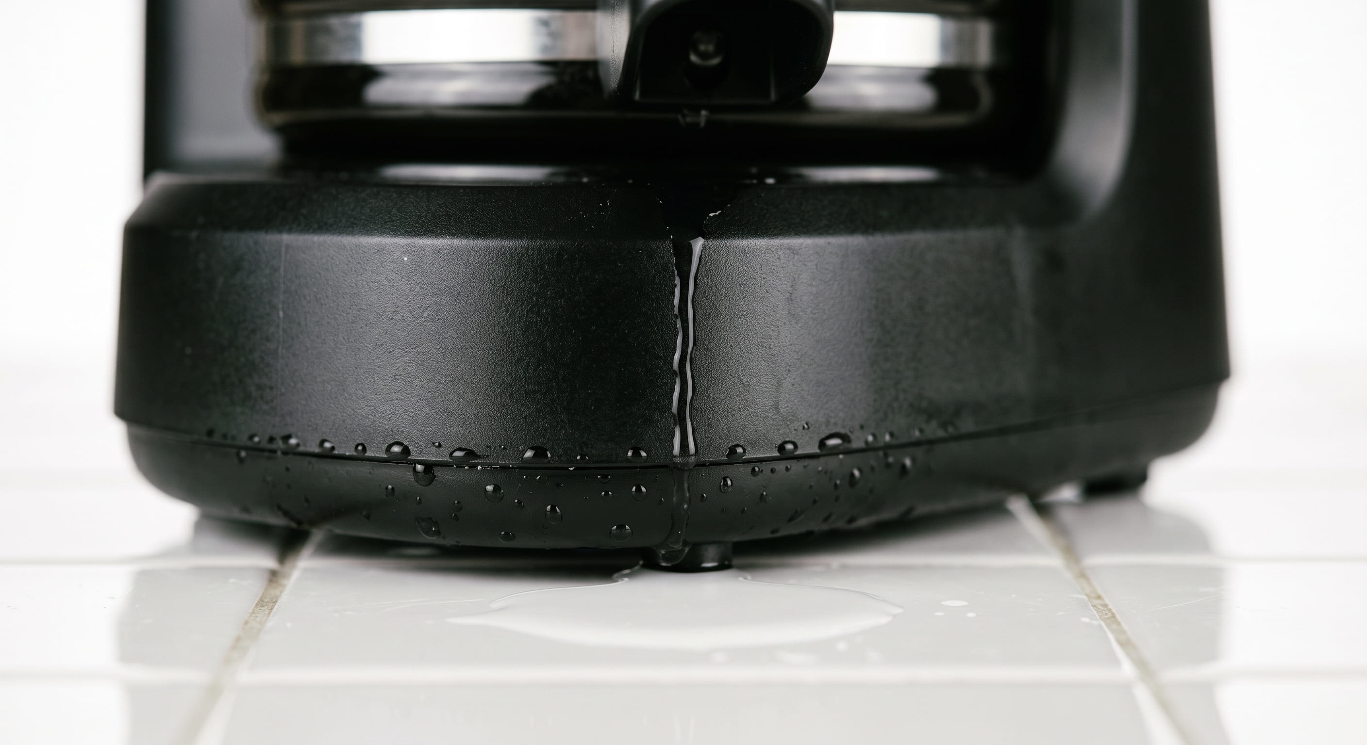 Water pooling on a kitchen counter directly beneath a drip coffee maker — illustrating a coffee maker leaking from the bottom near the heating element base