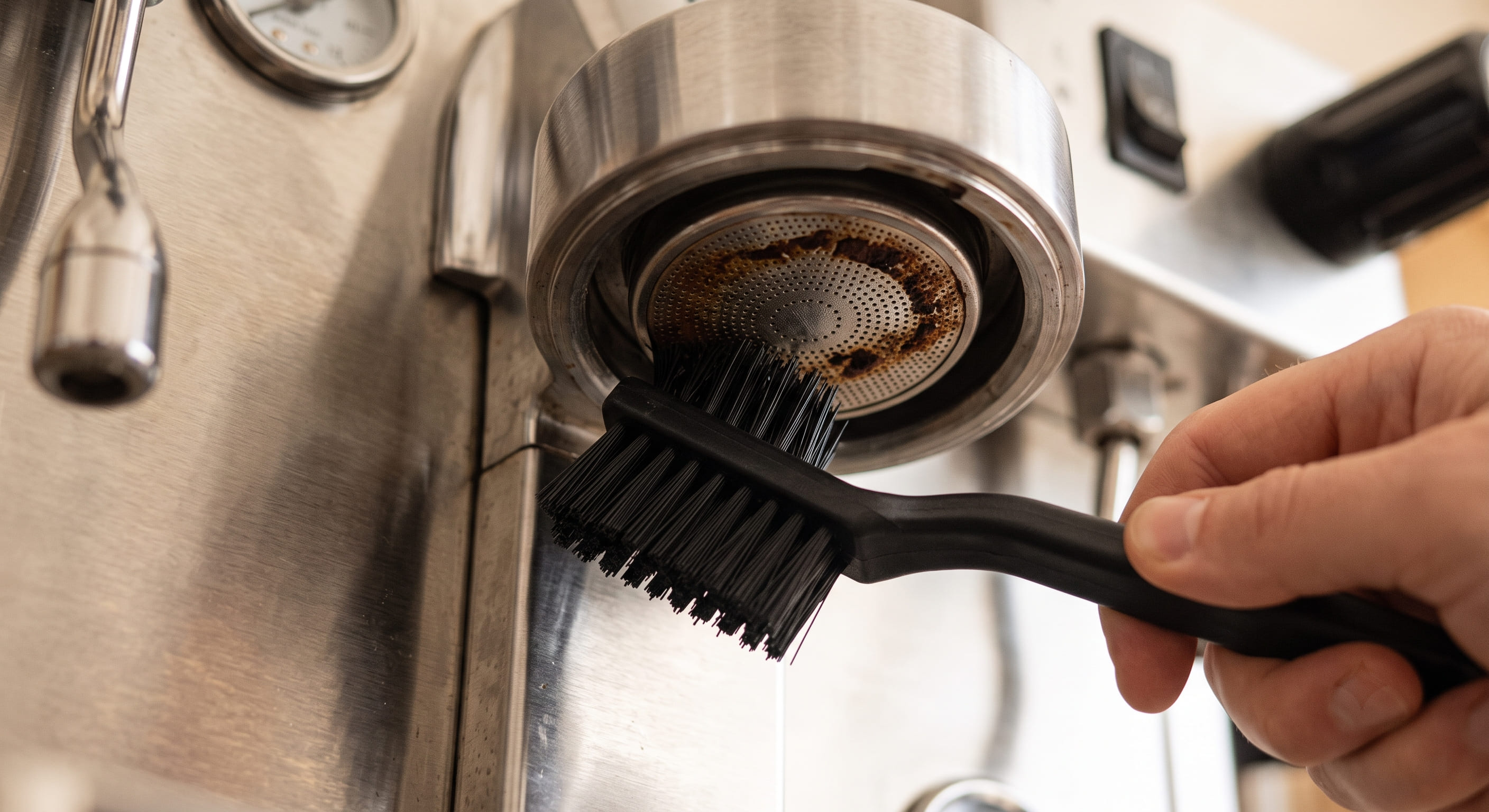 Group head shower screen removed and soaking in a cup of hot water with cleaning tablet — deep cleaning espresso machine group head to restore even water distribution and improve crema quality