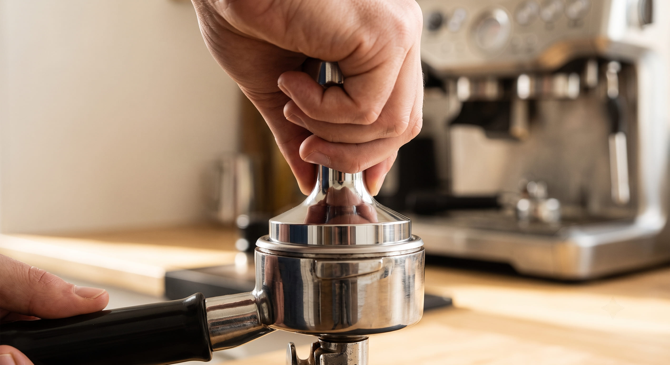 Barista pressing a flat tamper perfectly level into a portafilter basket filled with ground espresso coffee — demonstrating correct level tamping technique to prevent channelling and improve espresso crema