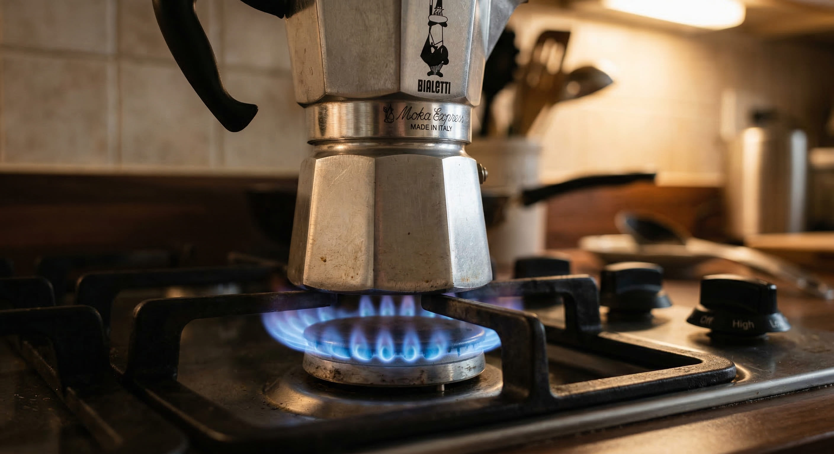 Close-up of a classic Bialetti Moka Express on a gas hob at correct medium-low heat — the blue flame just touching the base of the lower chamber, not licking up the sides, demonstrating correct bialetti technique heat management